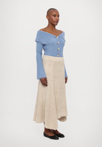Light blue knitted off-shoulder sweater with buttons, paired with a beige textured wrap skirt and black flats.