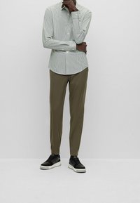 Lichtgroen geruit overhemd met knopen, slim fit, lange mouwen. Gecombineerd met olijfgroene taps toelopende broek en zwarte sneakers met witte zolen.