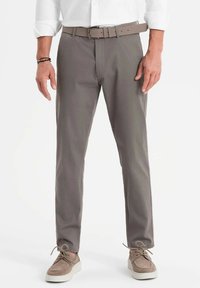 Pantaloni grigi con una finitura testurizzata, vestibilità dritta e una cintura abbinata. Indossati con scarpe in suede marroni chiari. Camicia bianca a maniche lunghe.