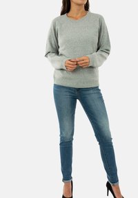 Svetlo siva jopica z rebrastimi manšetami in robom, v kombinaciji z oprijetimi modrimi kavbojkami in črnimi visokimi petami. Mehka, pletena tekstura z rahlim sijajem.