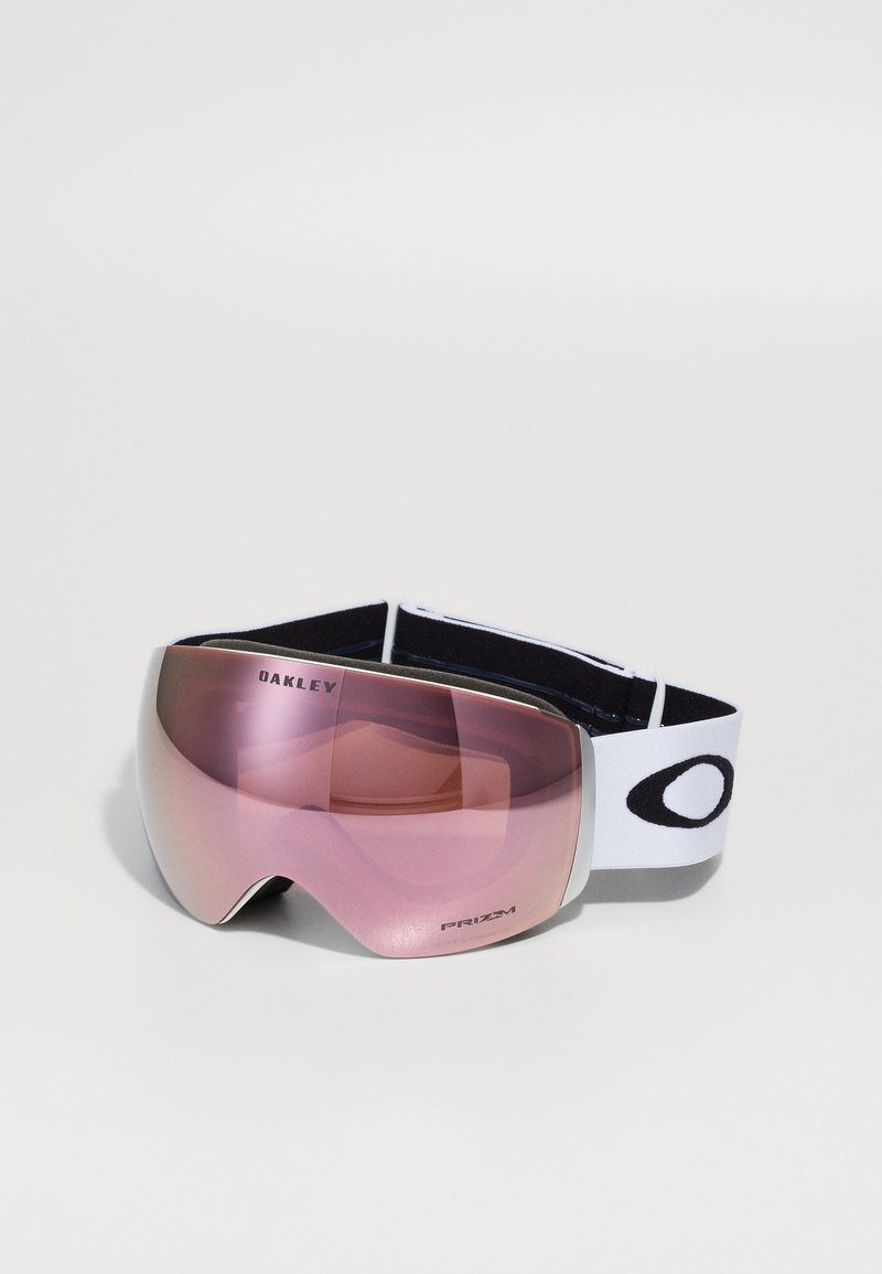 Rosa tippede skibriller med en stor buet linse, sort og hvid elastisk rem og sølvdetaljer; merkenavnet "Oakley" synlig.