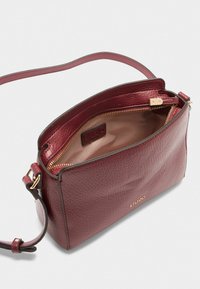 Borsa a tracolla in pelle bordeaux con finitura texturizzata, hardware dorato e chiusura con zip. L'interno presenta una fodera chiara e un logo.