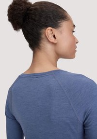 Langsleeve blauwe top met een zachte textuur, raglanmouwen en een ronde halslijn, gezien vanaf de achterkant.