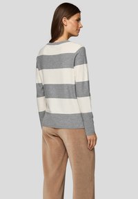 Grau-weiß gestreifter Pullover mit langen Ärmeln, rundem Ausschnitt und weicher Textur, kombiniert mit hellbraunen Cordhosen.