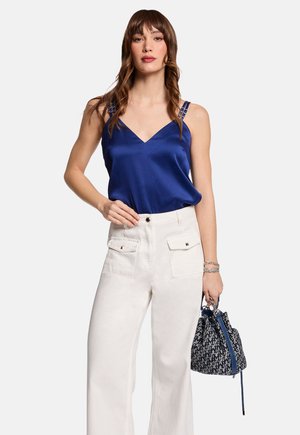 Camisole en satin bleu marine avec décolleté en V et bretelles détaillées, associée à un pantalon blanc taille haute avec poches avant et un sac à cordon.