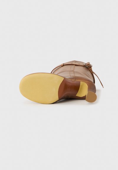 Brown leather ankle boot lying on its side showing smooth yellow rubber sole and small block heel on white background.