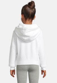 Hvit avkortet hettegenser med elastiske mansjetter og hem. Stoffet ser mykt og glatt ut, kombinert med grå leggings.