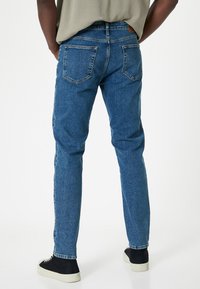 Jeans de mezclilla azul con un diseño de pierna recta, bolsillos traseros visibles y una cintura de altura media, combinados con zapatillas negras. Textura suave.