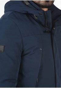 Marineblå isoleret jakke med hætte, udstyret med lynlås og trykknaplukninger, justerbare snore og en tekstureret inderside.