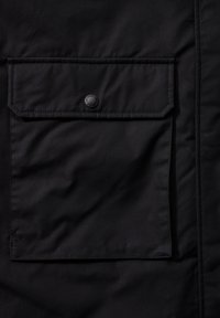 Černá prošívaná bunda s velkou přední kapsou se zapínáním na patent a hladkým textilním povrchem. Jednoduchý, funkční design.