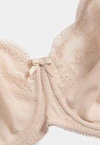 Soutien-gorge en dentelle beige avec motifs floraux, en tissu en mesh, bords festonnés et un petit nœud en satin au centre.