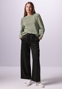 Ljusgrön långärmad tröja med puffärmar, som bärs med svarta vida cargobyxor med frontfickor och dragsko i midjan.