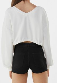 Vit croppad sweatshirt med V-ringning och elastisk nederkant, i kombination med högmidjade svarta shorts med bakfickor och en figurnära passform.