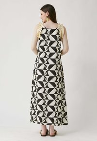 Abito lungo con un motivo geometrico in bianco e nero, dalla silhouette fluida e con accenti a volant crema a contrasto sulle spalle.