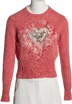 Pull en maille rouge avec un motif cœur blanc entouré de motifs floraux, associé à un pantalon blanc sur un mannequin.