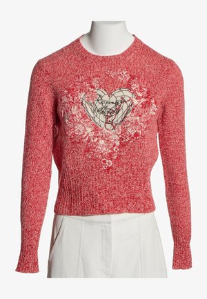 Pull en maille rouge avec un motif cœur blanc entouré de motifs floraux, associé à un pantalon blanc sur un mannequin.