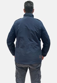 Giacca imbottita blu navy con colletto alto, design trapuntato e polsini elasticizzati; presenta un accento arancione vicino all'orlo.