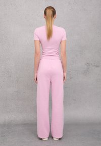 Camiseta ajustada rosa y pantalones de chándal de pierna ancha en un material suave y ligero. Diseño simple sin patrones ni adornos.