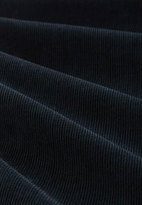 Ciemnoniebieska tkanina sztruksowa z widoczną fakturą prążków i miękkim wykończeniem, ułożona w fałdy, aby pokazać grubość i szczegóły wzoru.