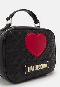 Svart vadderad handväska med röd hjärtapplikation och guldig "LOVE MOSCHINO" logoplått, med ett kort svart handtag och dragkedjestängning.