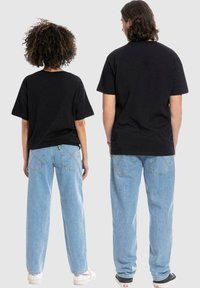 Zwarte katoenen t-shirts gecombineerd met lichtblauwe denim jeans, met een losse pasvorm en rechte broekspijpen, gezien vanuit de achterkant.