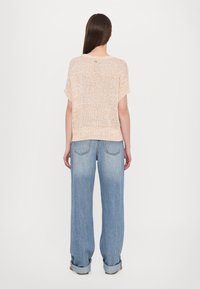 Lys beige strikket topp med korte ermer og en løs passform, kombinert med høyt liv og vide lyseblå jeans.