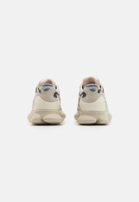 Beige sneakers med ett strukturerat tygöverdrag, gummisula och en rundad, bulformad design. Har en blå "CAMper"-logotyp baktill.