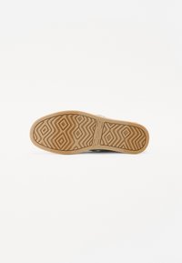Suela de zapato con goma texturizada, que presenta un patrón geométrico ondulado. El color es marrón claro con una base beige. Logo visible en el lateral.