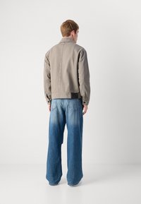 Grå jakke med en enkel design, knappdetaljer og en svakt cropped fasong; kombinert med vide lyseblå jeans med en falmet effekt.