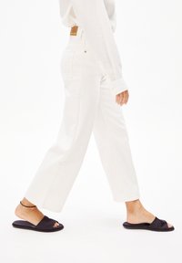 Jean large blanche à taille haute, assortie à des sandales à glissière noires avec une texture lisse et un design à bout ouvert.