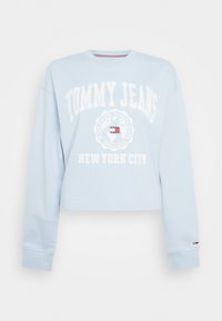 Felpa cropped a maniche lunghe di colore azzurro chiaro con il testo e il logo bianchi "Tommy Jeans New York City" al centro, polsini a coste e scollo tondo.