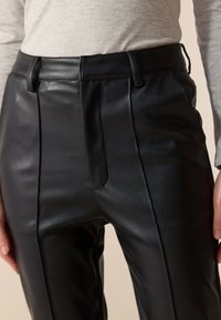 Schwarze Lederhose mit einem eleganten Design, ausgestattet mit vorderen Falten und gerade geschnittenem Bein. Glatte Textur und maßgeschneiderte Bunddetails.