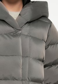 Grijze poffetermantel met capuchon, glanzende textuur en een gestikt ontwerp met zichtbare stiksels en een sluiting aan de voorkant.