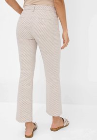 Gecombineerde crèmekleurige broek met een geometrisch ontwerp, middelhoge taille en uitlopende pijpen. Bevat twee achterzakken en een gladde stoftextuur.