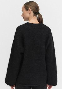 Svart, fluffig tröja med överdimensionerade ärmar, hög nacke och en avslappnad passform. Texturerad tyg med en mjuk, borstad yta.