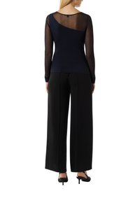 Marineblauwe top met transparante geribde lange mouwen en een effen lijfje, met een asymmetrisch ontwerp aan de achterkant. Gecombineerd met brede zwarte broek.