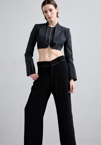 Black cropped jacket with a zip front and long sleeves, paired with high-waisted black wide-leg trousers featuring a folded waistband.