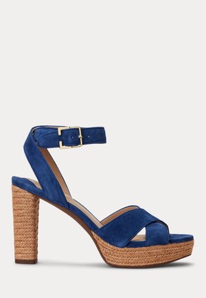 Blue suede high-heeled sandal with wide crossed straps, adjustable ankle strap, and a woven raffia platform. Gold buckle accents detail.