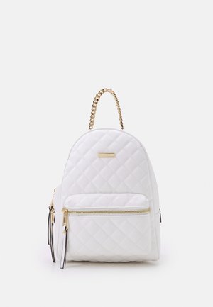 White quilted backpack with front zip pocket, gold chain handle, and gold brand plaque on smooth white background.