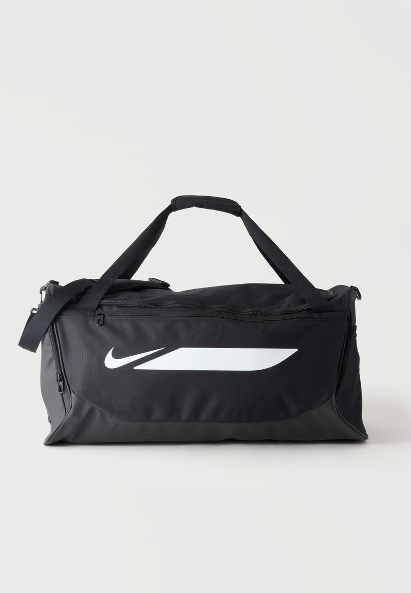 Μαύρη τσάντα Nike duffel με λευκό λογότυπο, διπλές λαβές και ρυθμιζόμενο ιμάντα ώμου σε απλό φωτεινό φόντο.