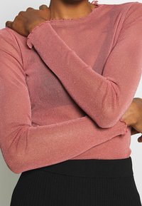 Häikäisevä, kiiltävä vaaleanpunainen pitkähihainen paita, jossa on frilla kauluksessa ja hihoissa; yhdistetty mustaan ribbitettuun hameeseen.