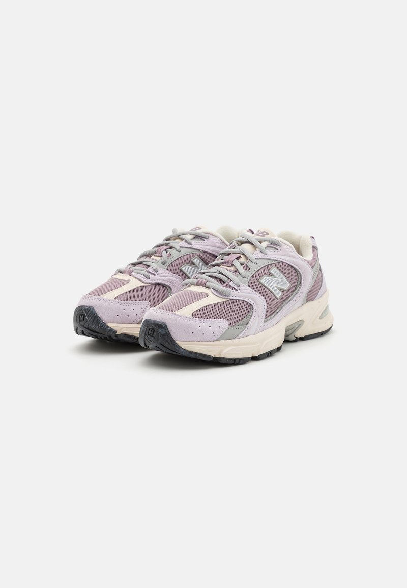 Paire de chaussures de course New Balance lavande et beige avec des accents gris et des semelles noires sur fond blanc.