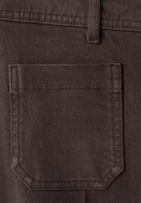 Primer plano de un bolsillo trasero de tela marrón oscuro en unos pantalones, con costuras visibles y un presilla para cinturón encima.