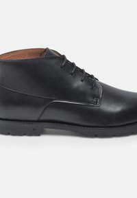 Bottines en cuir noir avec une texture lisse, dotées d'un bout rond, d'un design à lacets et d'un intérieur marron contrastant. Semelle en caoutchouc plate.
