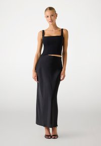 Schwarzes Cropped-Top mit quadratischem Ausschnitt und breiten Trägern, kombiniert mit einem fließenden schwarzen Maxirock. Glatte Textur, elegante Silhouette, minimale Details.