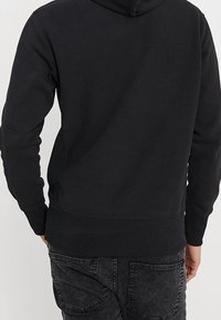Sudadera con capucha negra, mezcla de algodón, que cuenta con una capucha, puños y dobladillo acanalados. Textura suave con costuras mínimas y sin logotipos visibles.