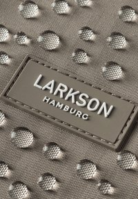 Tessuto grigio con una superficie testurizzata, caratterizzato da gocce d'acqua in rilievo e un'etichetta rettangolare con la scritta "LARKSON HAMBURG" in bianco.