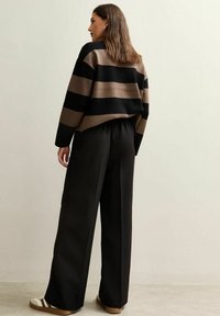 Suéter a rayas en negro y beige con un corte holgado, combinado con pantalones negros de cintura alta y zapatillas beige informales. Textura suave.