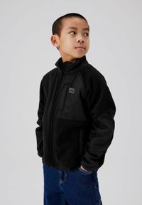 Veste en polaire noire avec un col haut, une fermeture éclair et une poche poitrine avec un logo. Manches lisses avec une texture contrastante.