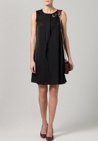 Vestito nero senza maniche con dettagli in pizzo sulle spalle, design drappeggiato e gonna a campana. Abbinato a una borsa a tracolla bordeaux.